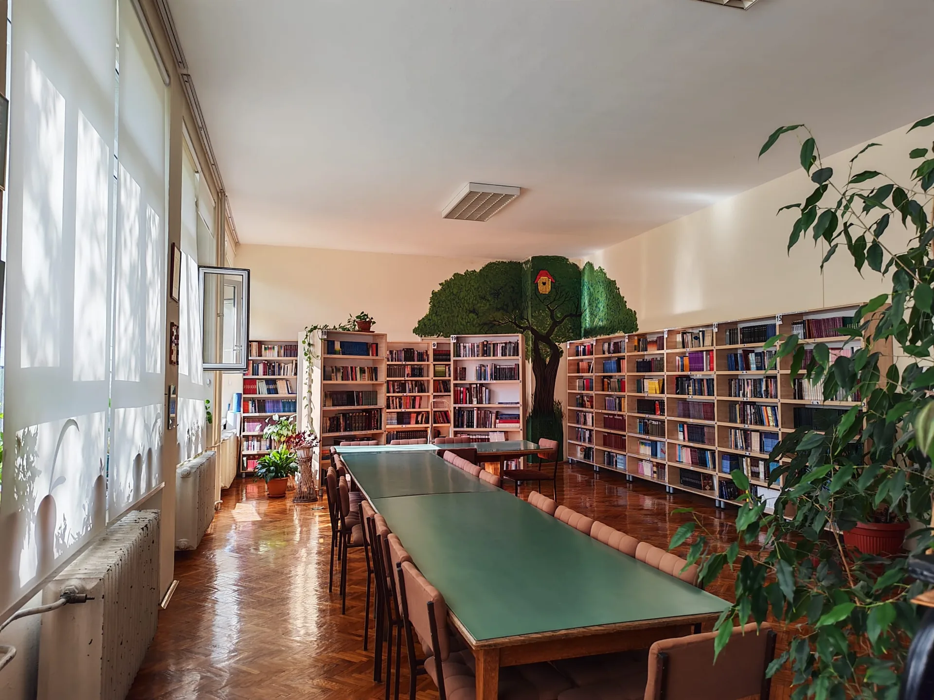 Читаонице библиотеке са зеленим столовима уз осликан зид